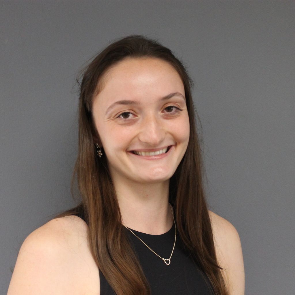 young woman with long brown hair, slight smile, wearing a black sleeveless shirt