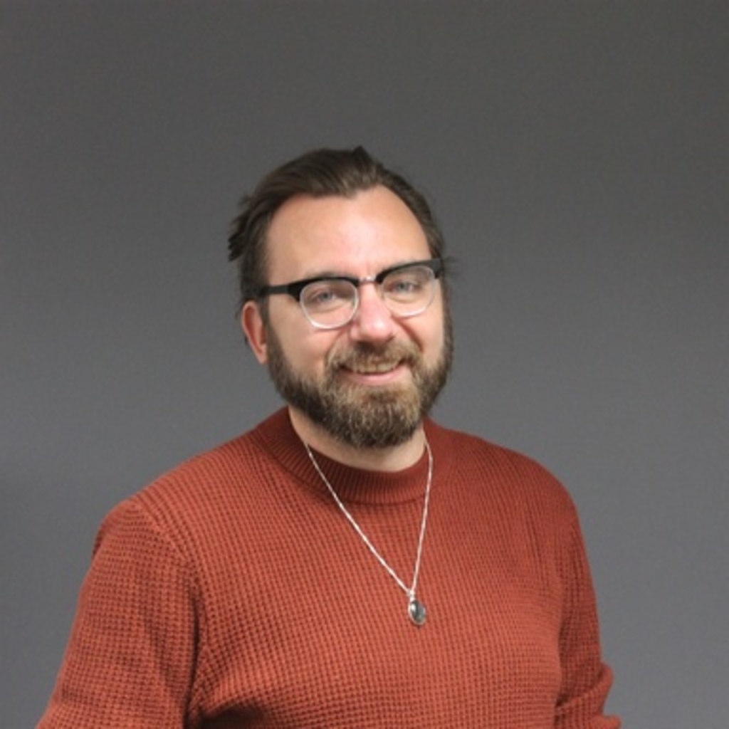 young man with long hair, wearing glasses, orange shirt