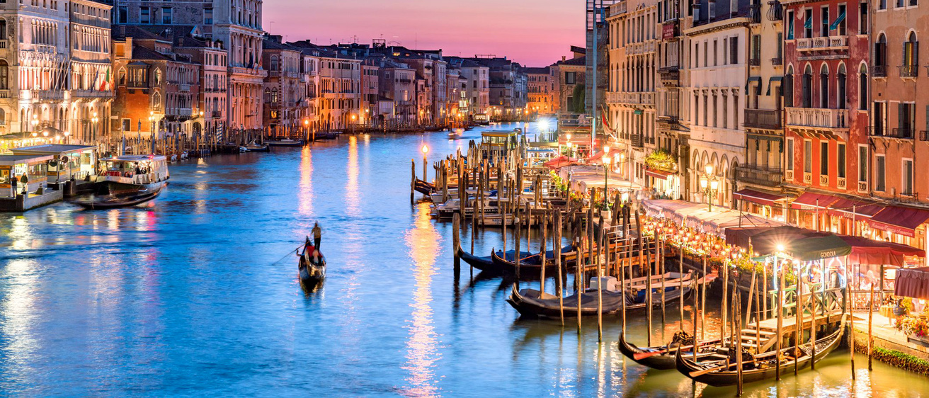 A gondolier navigates along Venice's Grand Canal at sunset.