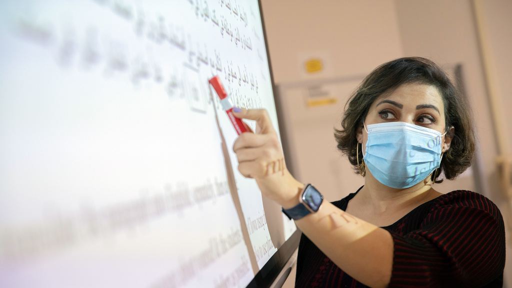 A mask-wearing instructor pointing to a lesson on the Arabic language.