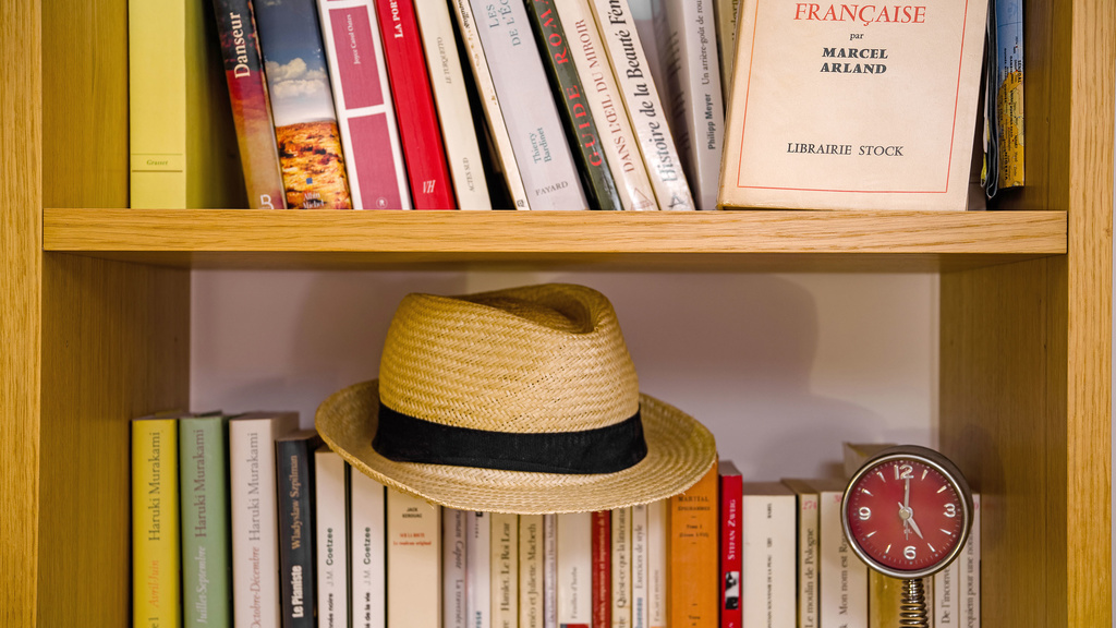 A hat and a collection of French books in a bookcase.