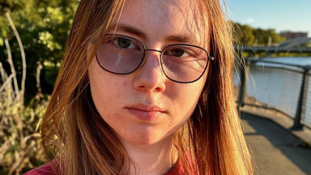 young person, shoulder length brownish hair, wearing glasses, red shirt