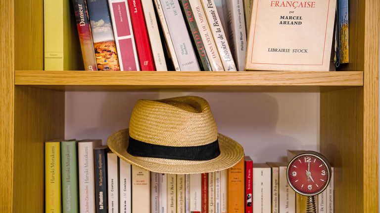 A hat and a collection of French books in a bookcase.